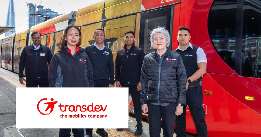 A group of six people in Transdev uniforms stand in front of a red tram with a Transdev logo and slogan, "the mobility company," displayed.