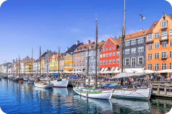 Colorful buildings line the waterfront at Nyhavn in Copenhagen, with boats docked along the canal under a clear blue sky.