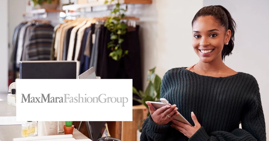 Smiling woman in a clothing store holding a phone, with racks of clothes in the background and a MaxMara Fashion Group logo.