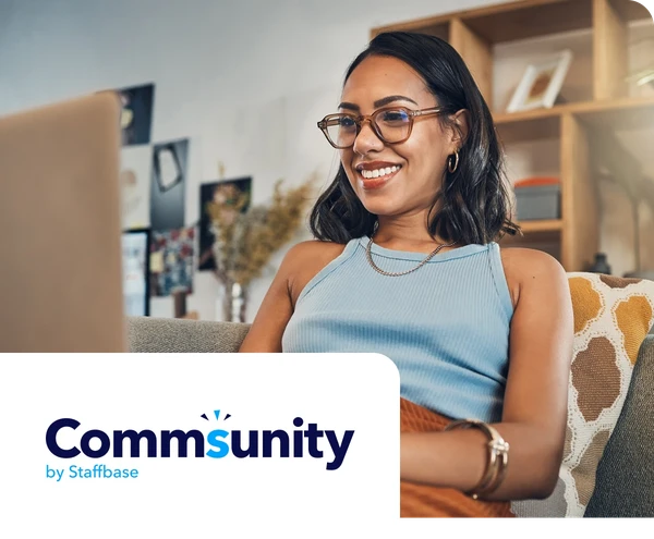 Smiling woman with glasses works on a laptop at home, sitting on a couch with a decorative cushion.