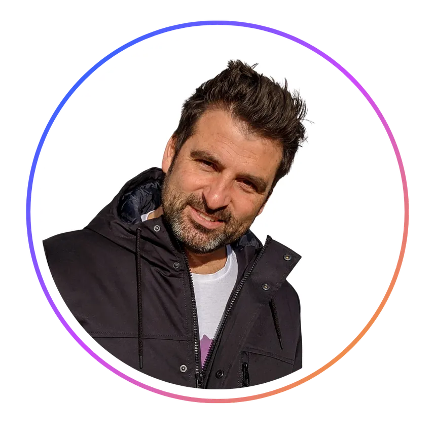 Man with dark hair and beard, wearing a black jacket, smiling at the camera. Circular frame with a gradient border.