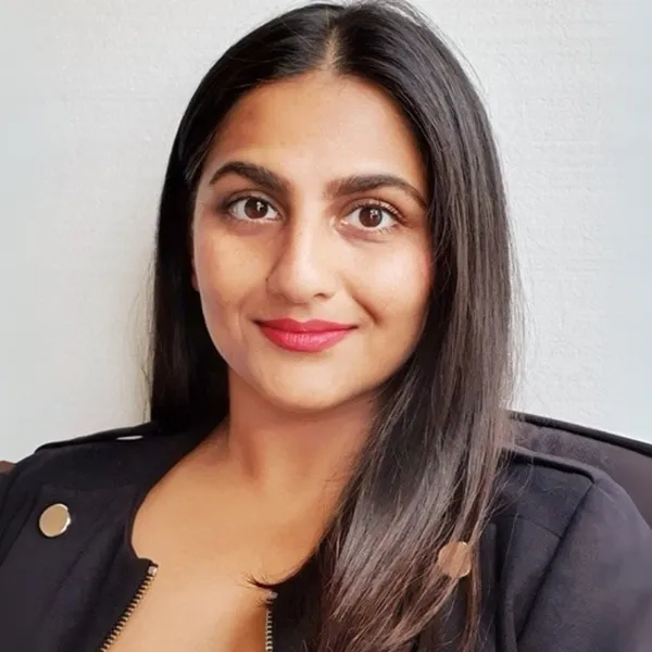 A woman with long dark hair and a black jacket smiles softly, sitting against a plain white background.