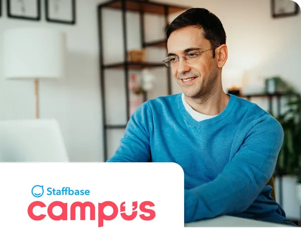 Man in a blue sweater working on a laptop at home, with "Staffbase Campus" logo in the foreground.