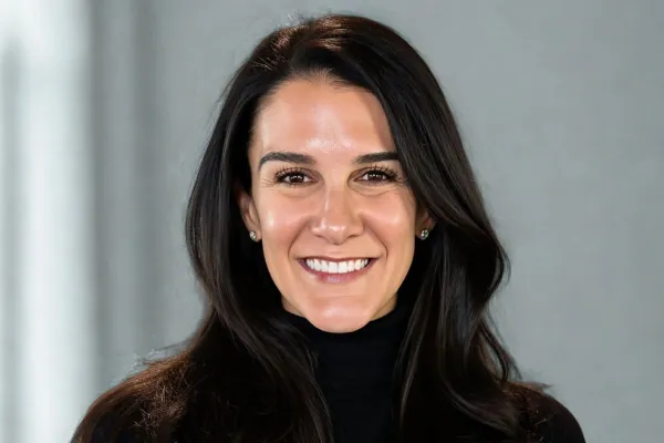 Smiling woman with long dark hair, wearing a black turtleneck, against a neutral background.