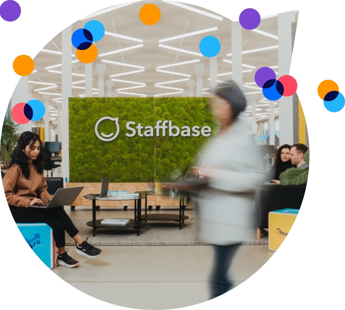 Modern office lobby with a green wall displaying "Staffbase." People are sitting and walking, some using laptops. Bright, colorful circles overlay.