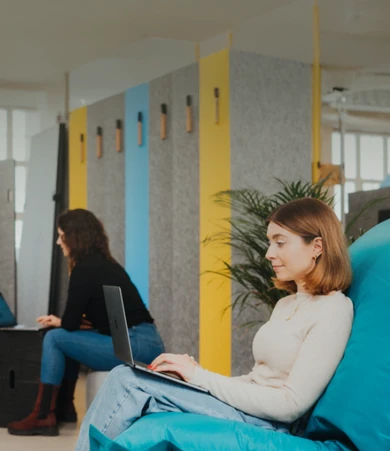 Vier junge Kolleginnen sitzen gemeinsam an einem Tisch, lachen und unterhalten sich konzentriert während sie an einem Laptop arbeiten.*