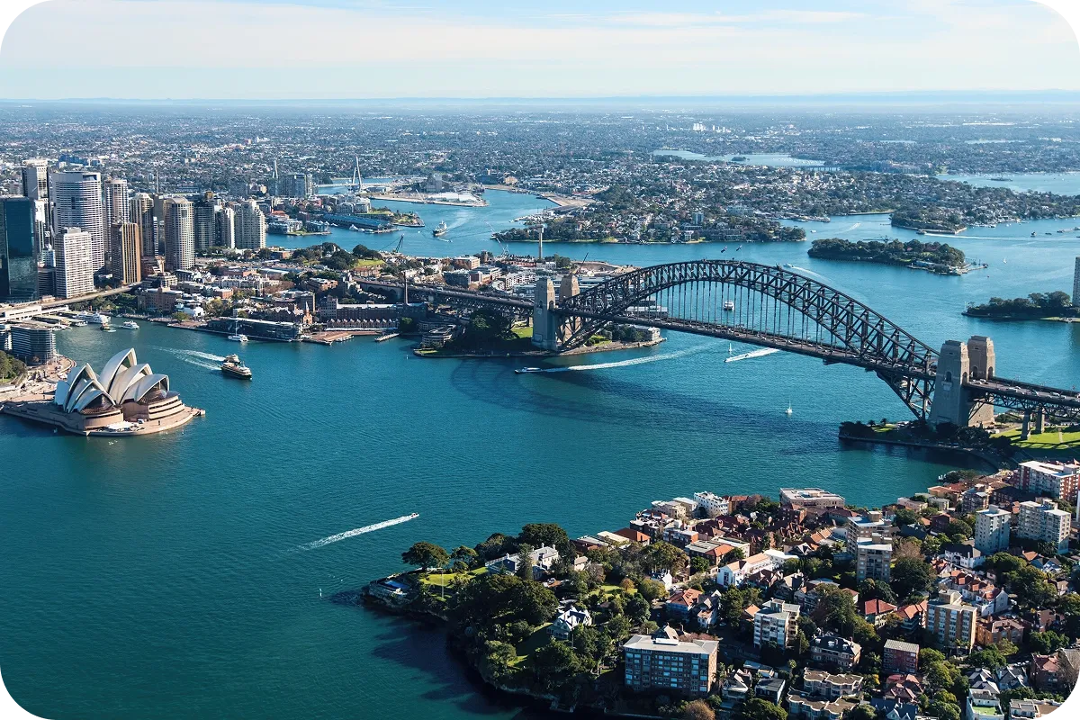 Aerial view of Sydney Harbour showing the Sydney Opera House, Harbour Bridge, and surrounding cityscape with boats on the water.