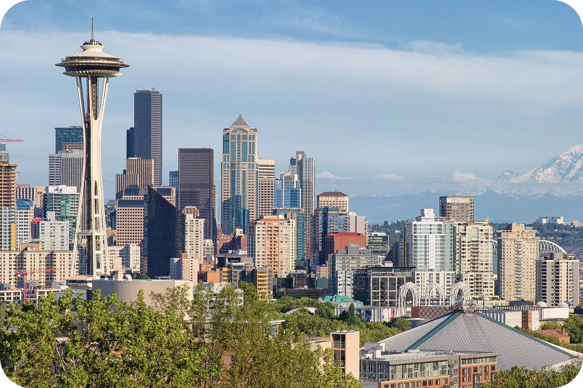 Seattle skyline with the Space Needle, diverse skyscrapers, and Mount Rainier in the background under a clear blue sky.