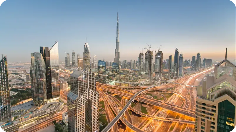 Dubai skyline at dusk featuring the Burj Khalifa and illuminated highway interchanges.