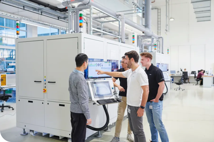 Four people in a modern lab setting discuss data on a monitor attached to a large, white industrial machine.