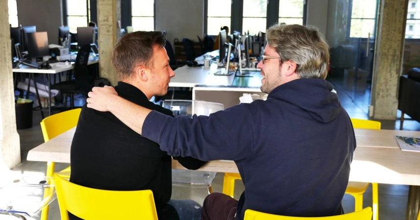 two men embrace each other in a friendly manner in an office setting