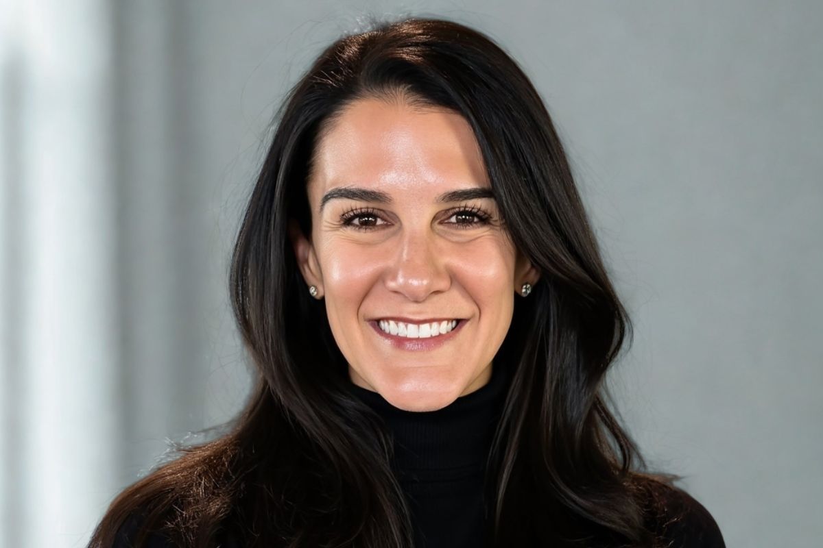 Smiling woman with long dark hair, wearing a black turtleneck, against a neutral background.